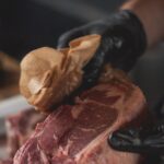 Le métier de boucher, ces gestes qui font toute la différence Mains gantées d'un boucher parant une pièce de viande de bœuf