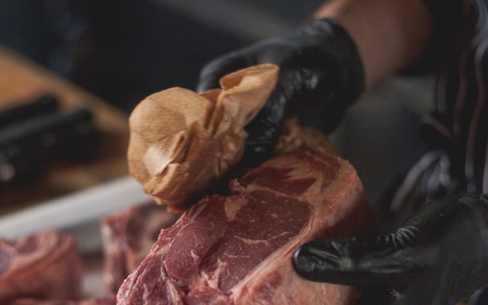 Mains gantées d'un boucher parant une pièce de viande de bœuf