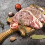 Le porc noir de Bigorre, la renaissance d'une race qu'on avait laissée mourir Côtes de porc crues sur une planche en bois avec du romarin et des tomates