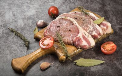 Le porc noir de Bigorre, la renaissance d'une race qu'on avait laissée mourir Côtes de porc crues sur une planche en bois avec du romarin et des tomates