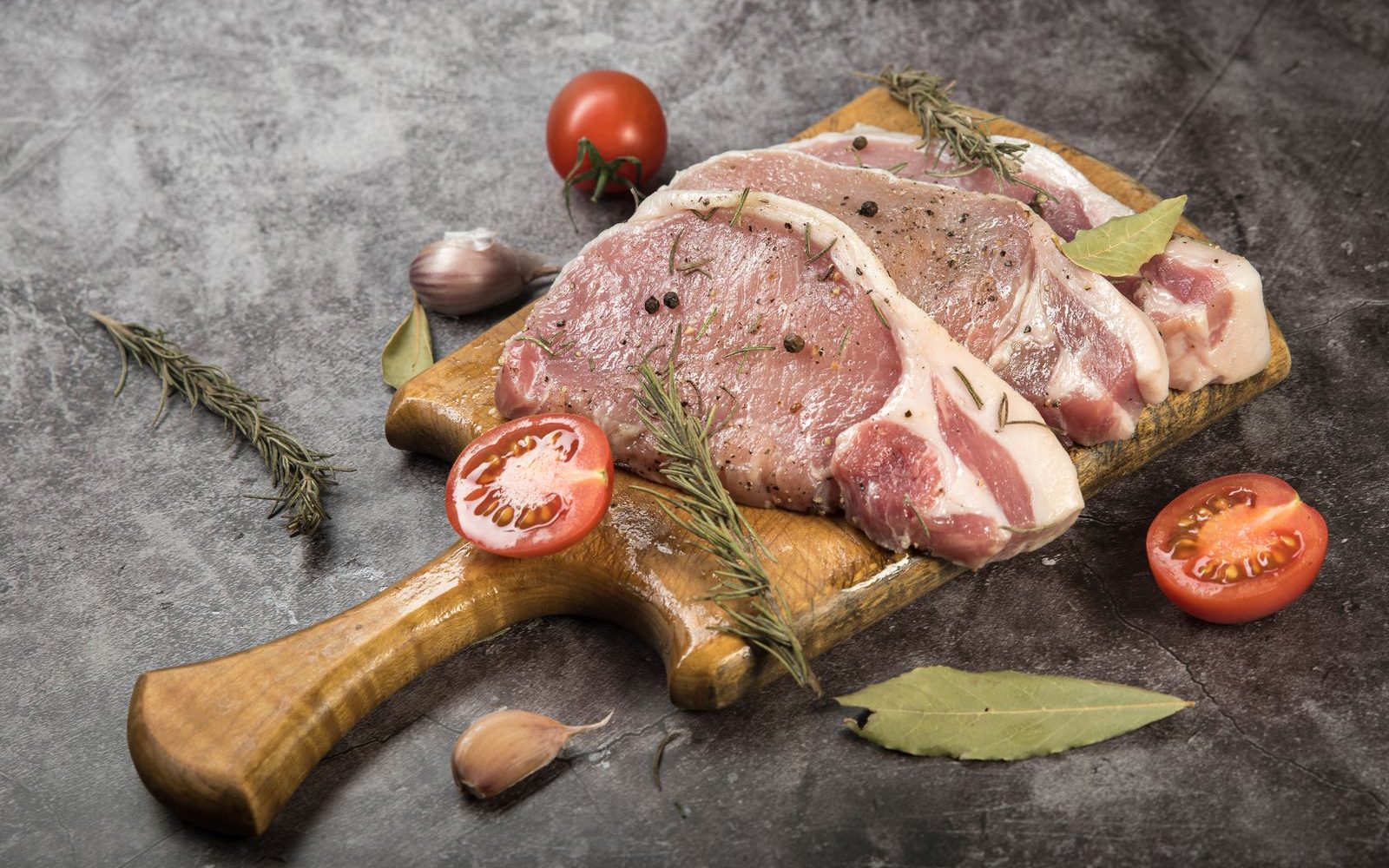 Côtes de porc crues sur une planche en bois avec du romarin et des tomates