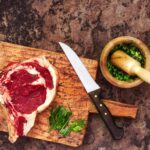 Cuire une côte de bœuf : la méthode qui marche à tous les coups Entrecôte de bœuf crue sur une planche avec un couteau de boucher et des herbes