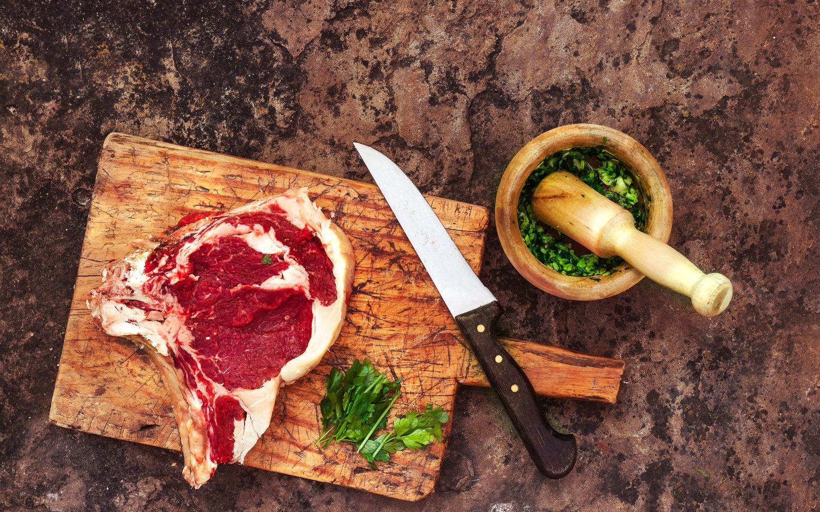 Entrecôte de bœuf crue sur une planche avec un couteau de boucher et des herbes