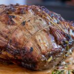 Cuisson basse température : le guide des viandes qui demandent du temps Rôti de bœuf ficelé et doré au four, garni d'herbes