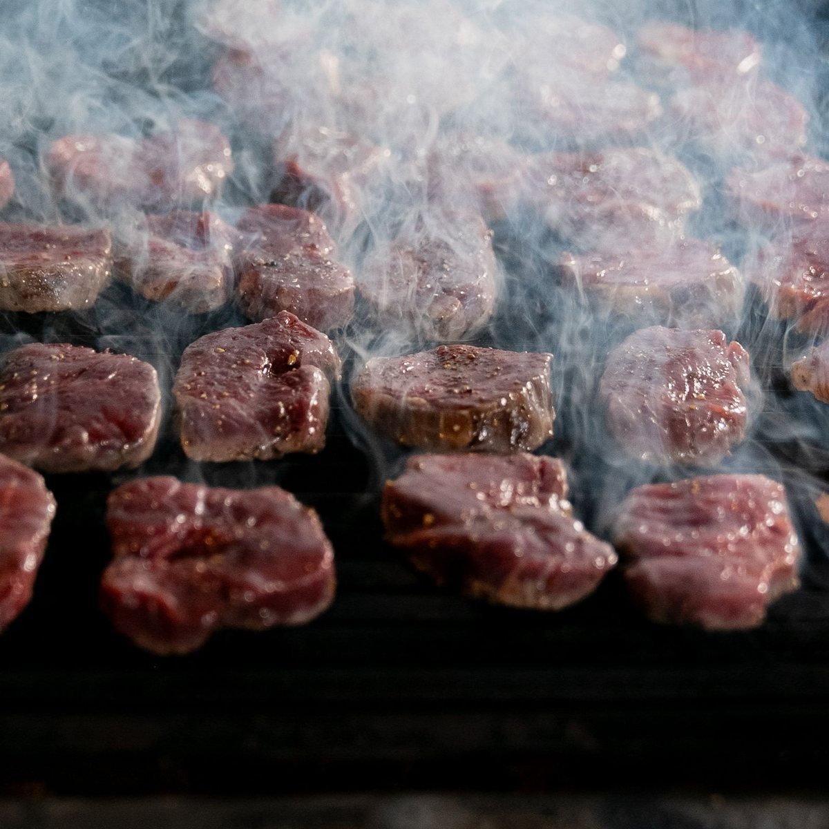 Steaks de bœuf en train de griller sur un barbecue fumant